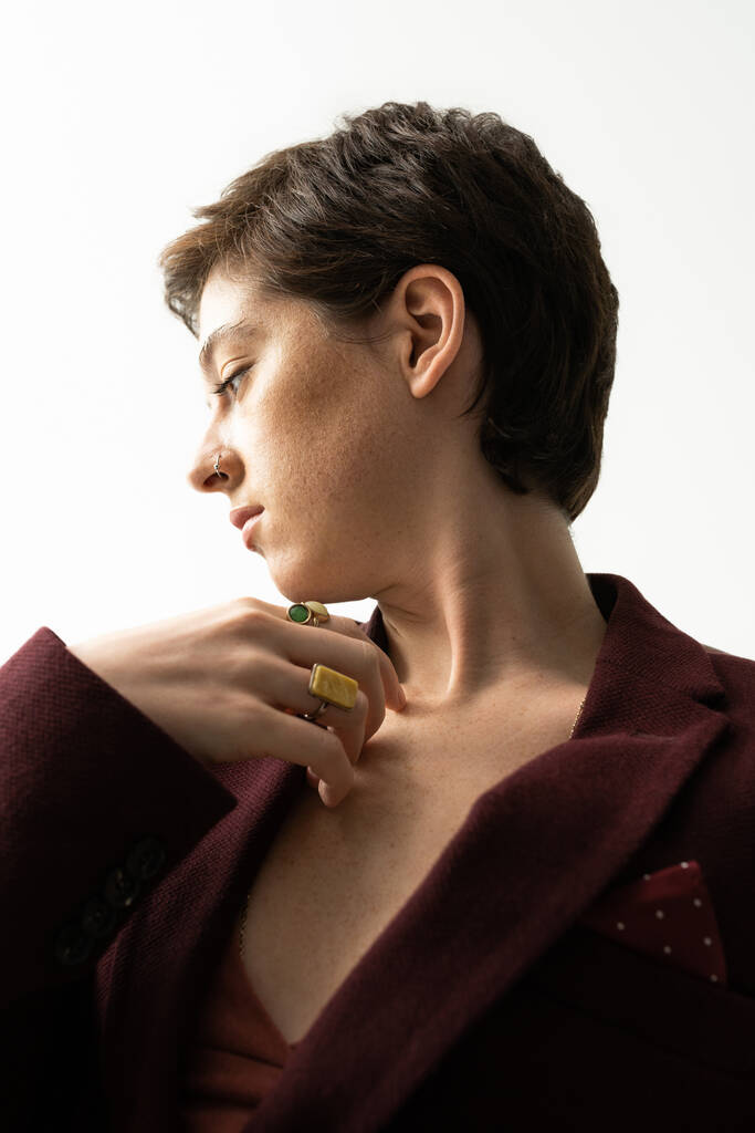 mulher sensual e sonhadora em blazer e anéis de dedo posando com a mão perto do peito em fundo cinza - Foto, Imagem