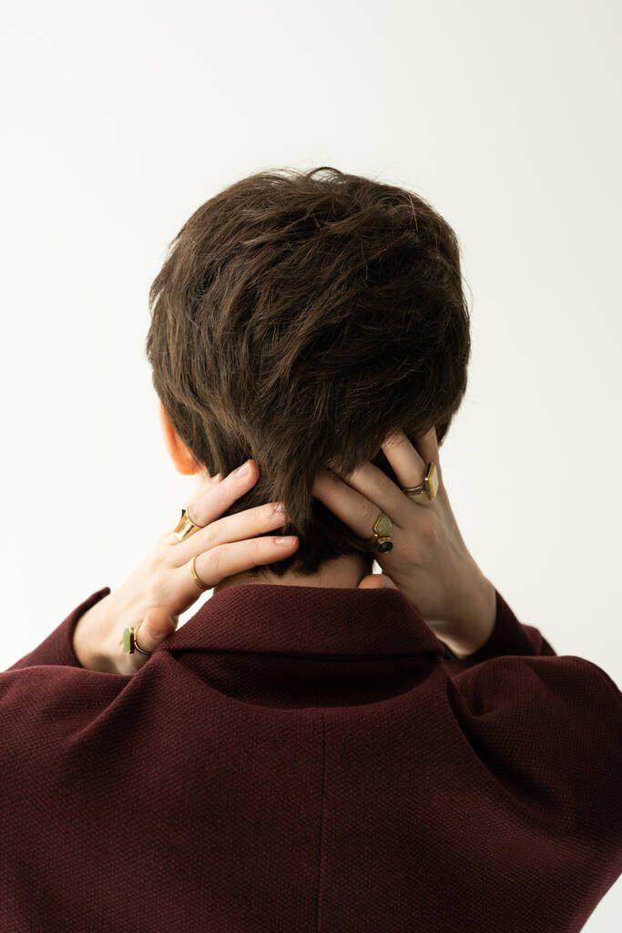 back view of brunette short haired woman in finger rings posing with hands behind neck isolated on grey - Photo, Image