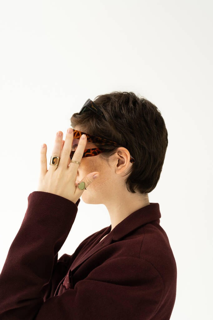 boční pohled na brunetky krátké vlasy žena v prstenech prsteny na sobě několik slunečních brýlí izolovaných na šedé - Fotografie, Obrázek