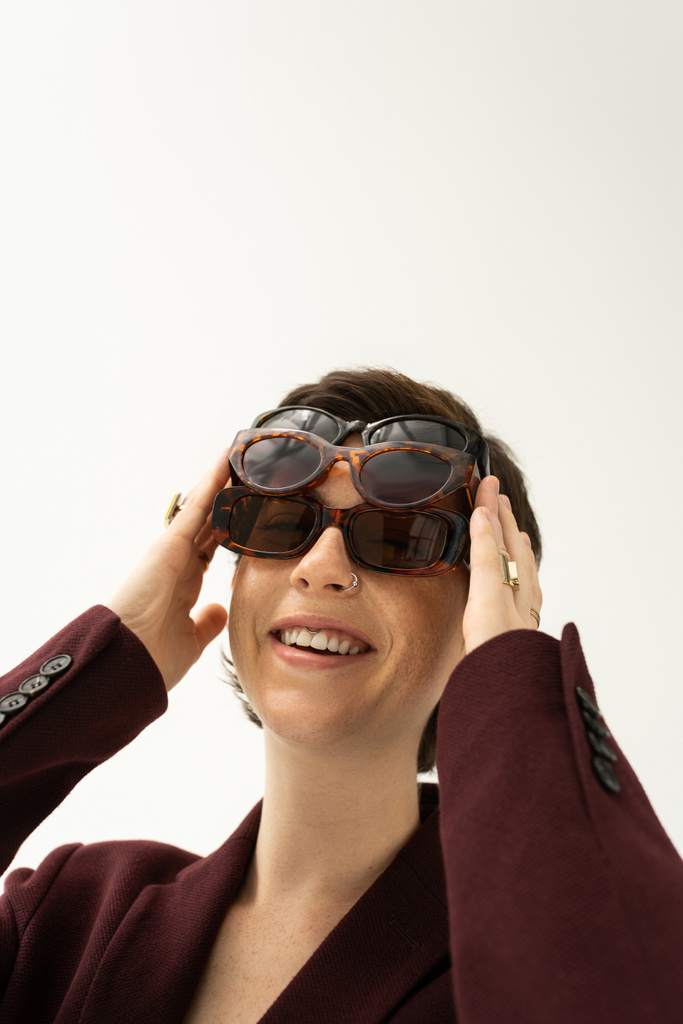 fiatal és gondtalan nő, különböző napszemüveget visel, szürkén elszigetelve - Fotó, kép
