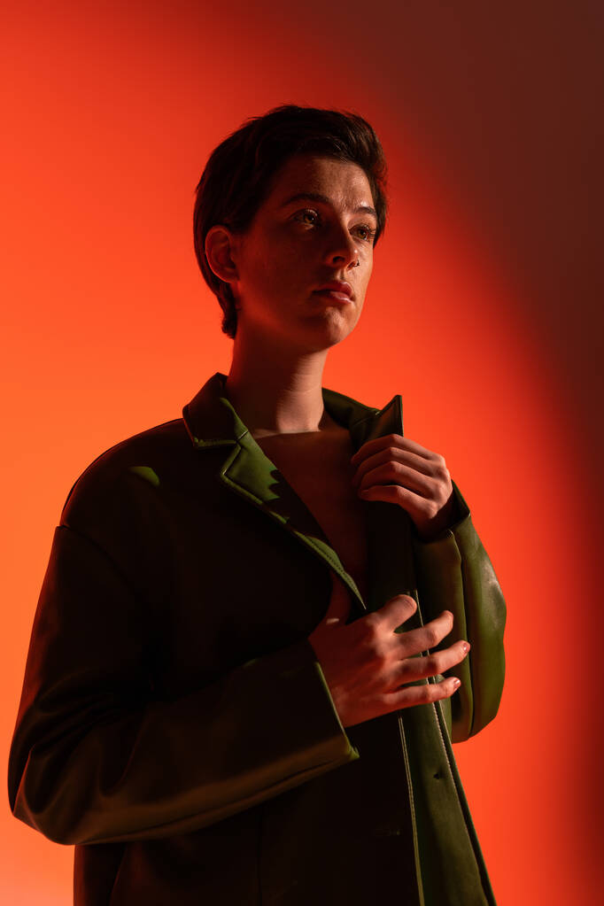 modische Frau in grüner Lederjacke schaut auf orangefarbenem Hintergrund weg - Foto, Bild