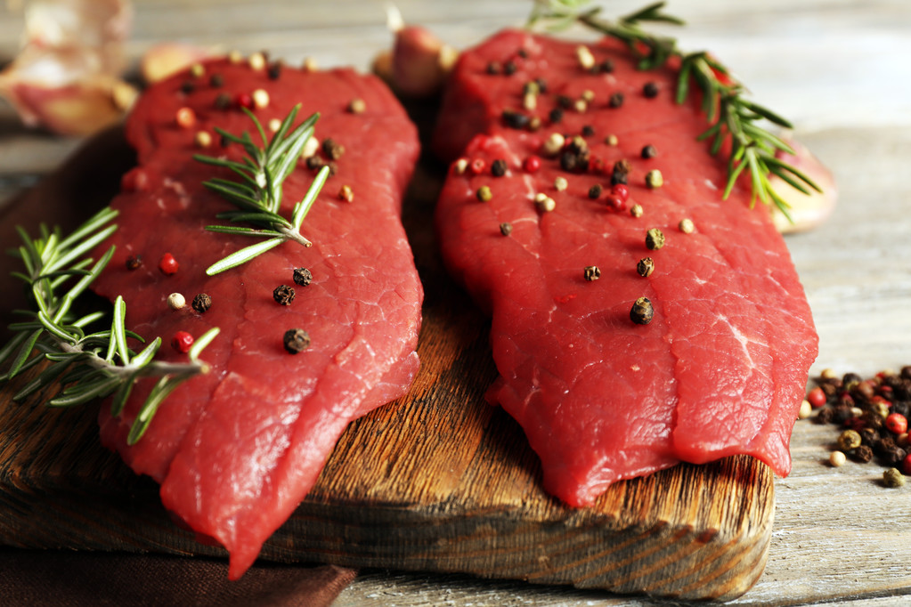 Rauwe biefstuk met rozemarijn en specerijen op snijplank op houten achtergrond - Foto, afbeelding