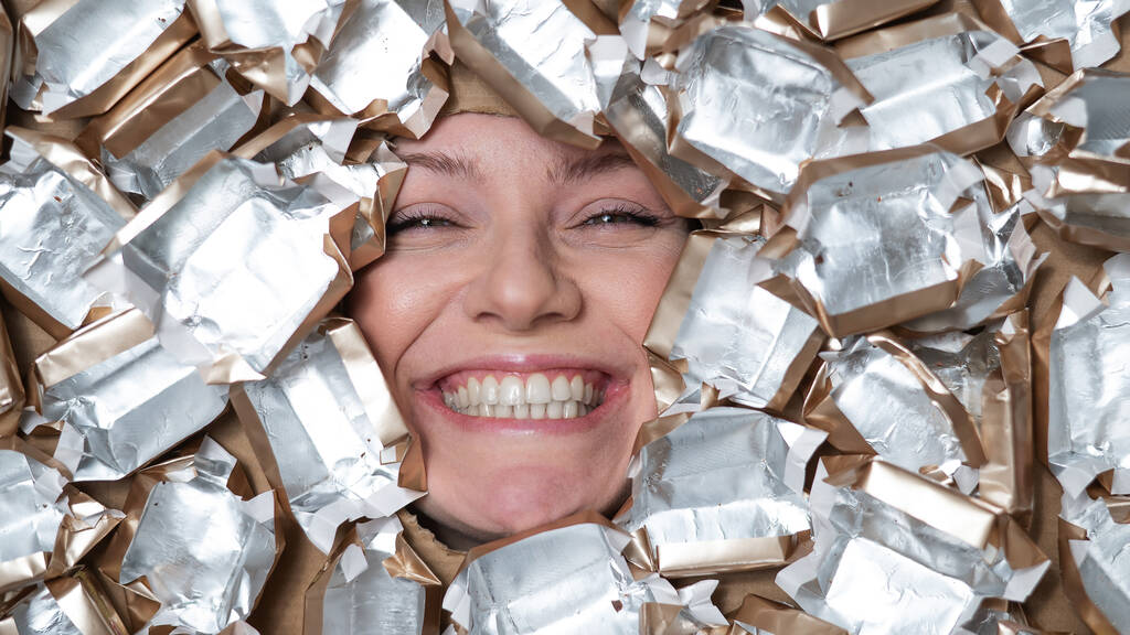 Il volto di una donna caucasica circondata da involucri di caramelle - Foto, immagini