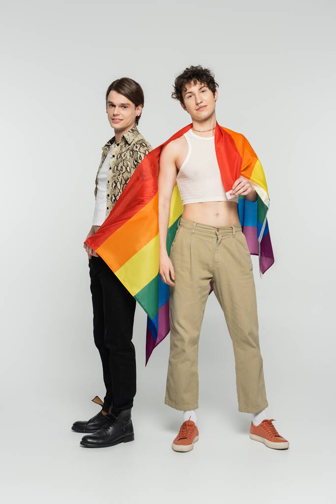pełna długość modnych partnerów panseksualnych z flagą lgbt patrząc w kamerę stojąc na szarym tle - Zdjęcie, obraz
