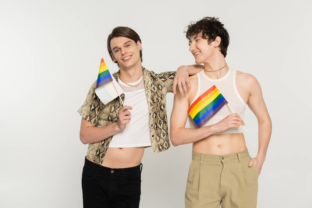 Neşeli ve şık biseksüel modeller Gri üzerinde küçük lgbt bayraklarıyla poz veriyorlar - Fotoğraf, Görsel