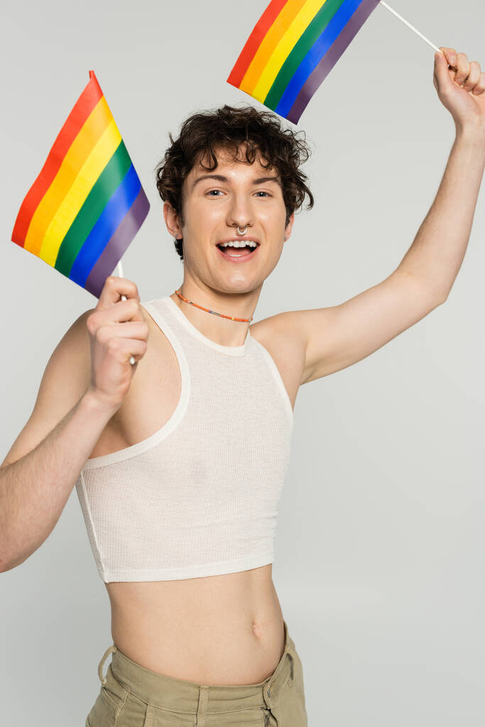 carefree bigender person in crop top standing with small lgbt flags isolated on grey - Photo, Image