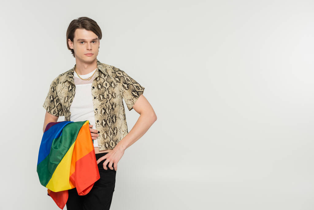 κομψό pansexual μοντέλο με lgbt σημαία στέκεται με το χέρι στο ισχίο και κοιτάζοντας κάμερα απομονώνονται σε γκρι - Φωτογραφία, εικόνα