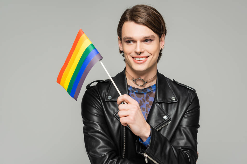 heureux et élégant pansexuel personne en cuir noir veste tenant petit drapeau lgbt isolé sur gris - Photo, image