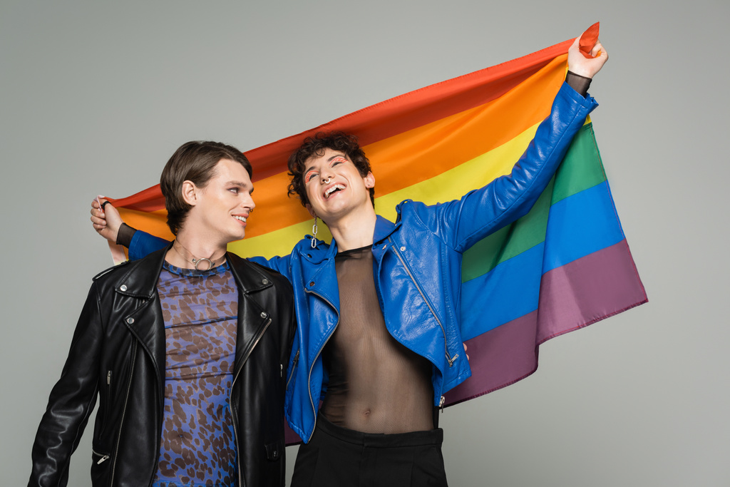 persona despreocupada más grande en chaqueta de cuero azul con bandera del arco iris cerca de pareja de moda aislado en gris - Foto, Imagen