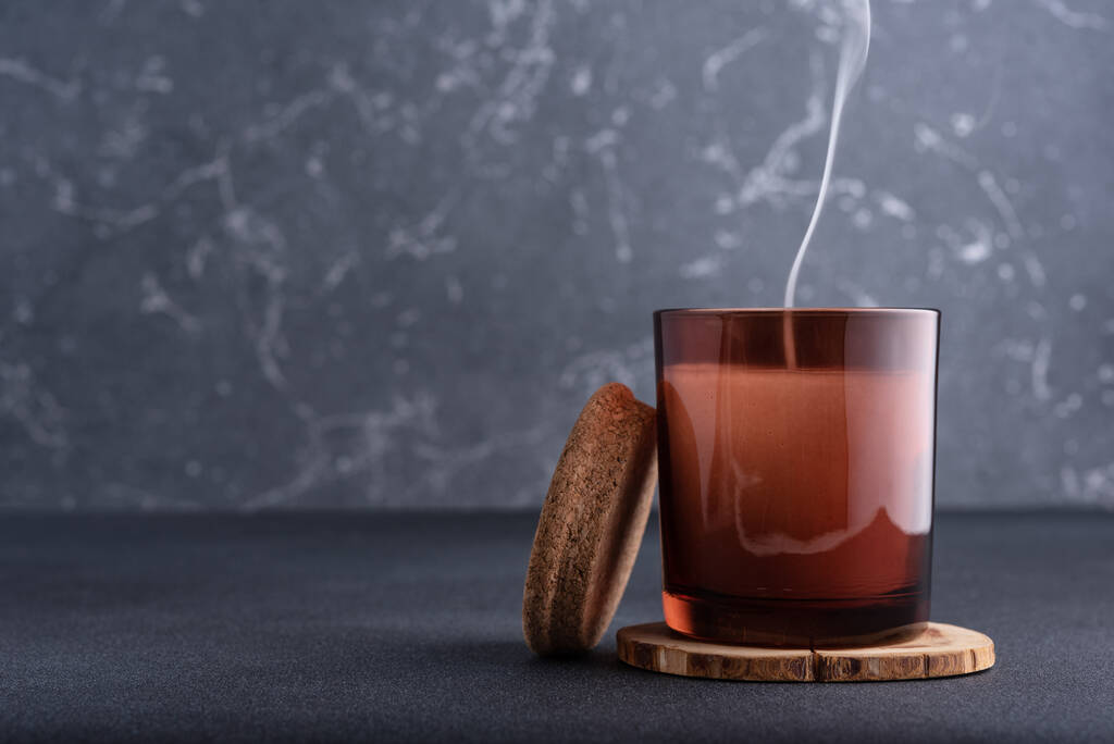 Затишна свічка в коричневій скляній банці з димом на темному фоні
 - Фото, зображення