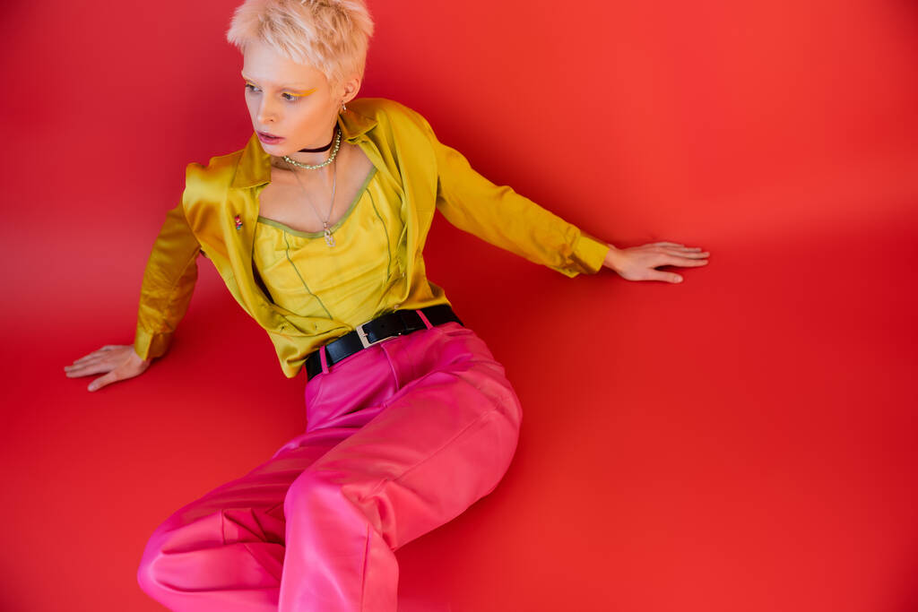 high angle view of blonde albino model in trendy clothes posing on carmine pink  - Photo, Image