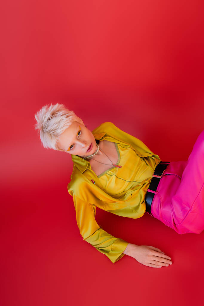 vista aerea del giovane modello albino in camicetta alla moda e pantaloni in posa sul carminio rosa  - Foto, immagini