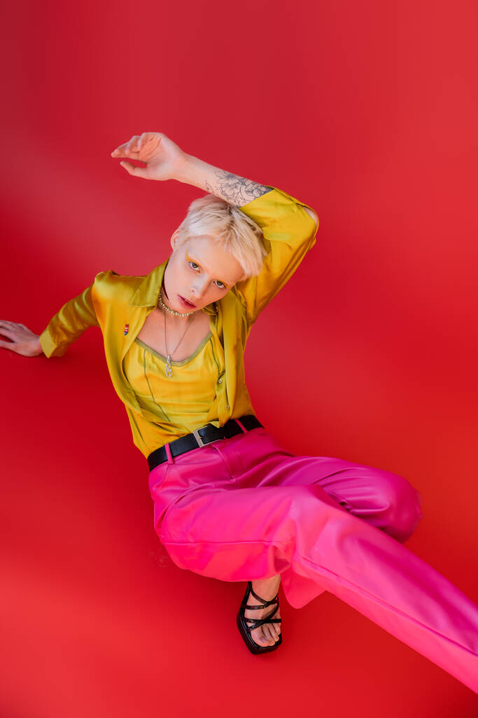 albino woman with blonde hair posing with raised tattooed hand on carmine pink  - Photo, Image