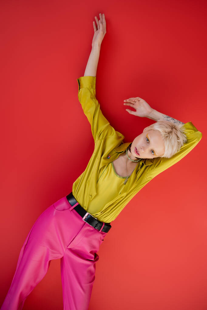 Albino γυναίκα με ξανθά μαλλιά και τατουάζ στο χέρι θέτει σε Carmine ροζ  - Φωτογραφία, εικόνα