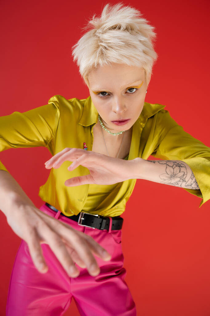 high angle view of albino woman with tattoo looking at camera while posing on carmine pink  - Photo, Image