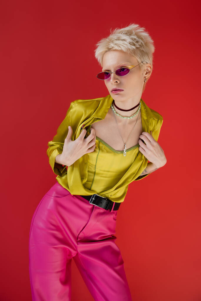 Parlak kıyafetli, dövmeli albino model ve Carmine Pembe 'de poz veren moda güneş gözlüğü.  - Fotoğraf, Görsel