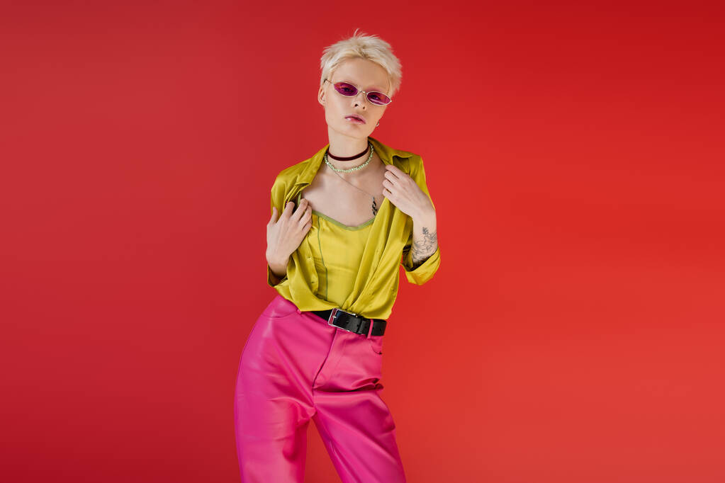 tätowiertes Albino-Model in stylischem Outfit und trendiger Sonnenbrille posiert auf karminrosa Hintergrund  - Foto, Bild