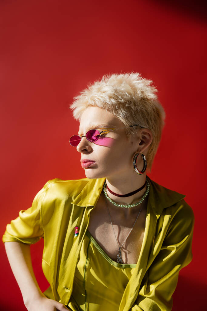 солнечный свет на лице модели альбиноса в стильных солнцезащитных очках и блузке, позирующих на розовом фоне  - Фото, изображение