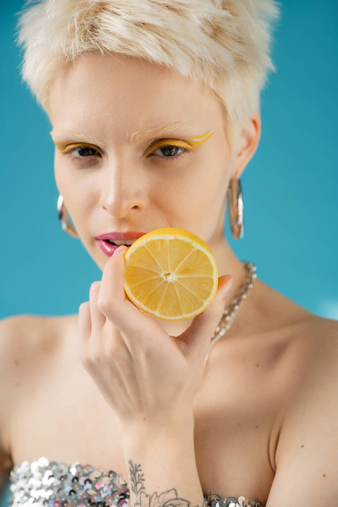 mujer albina rubia con hombros desnudos sosteniendo la mitad de limón en azul  - Foto, imagen