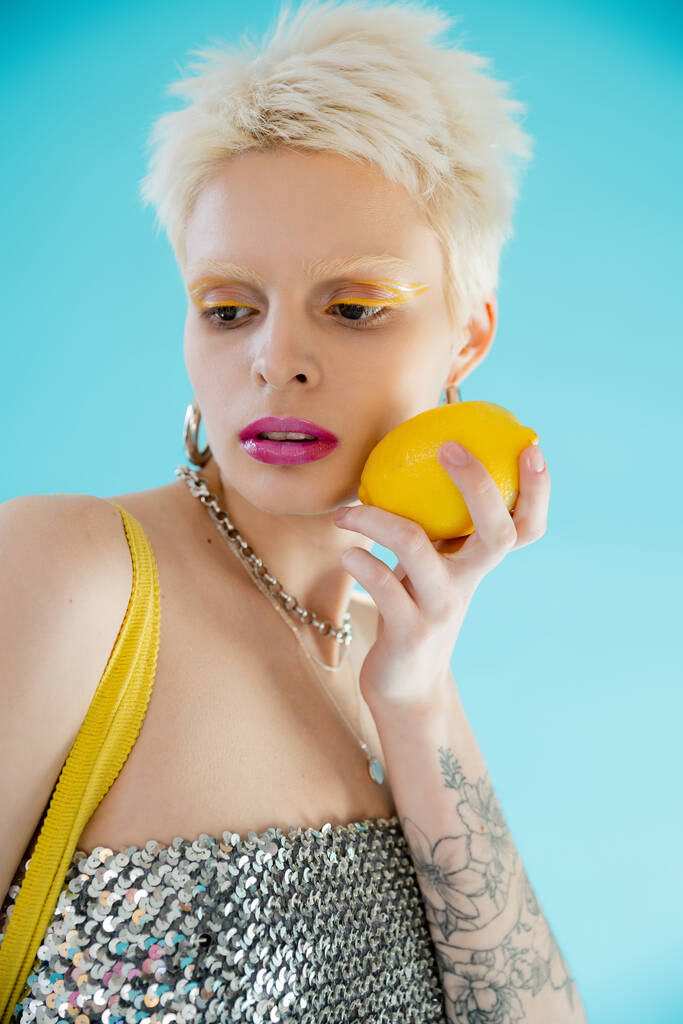 タトゥーのある女性で光沢のあるトップでスパンコールを保持しています熟したレモンオンブルー  - 写真・画像