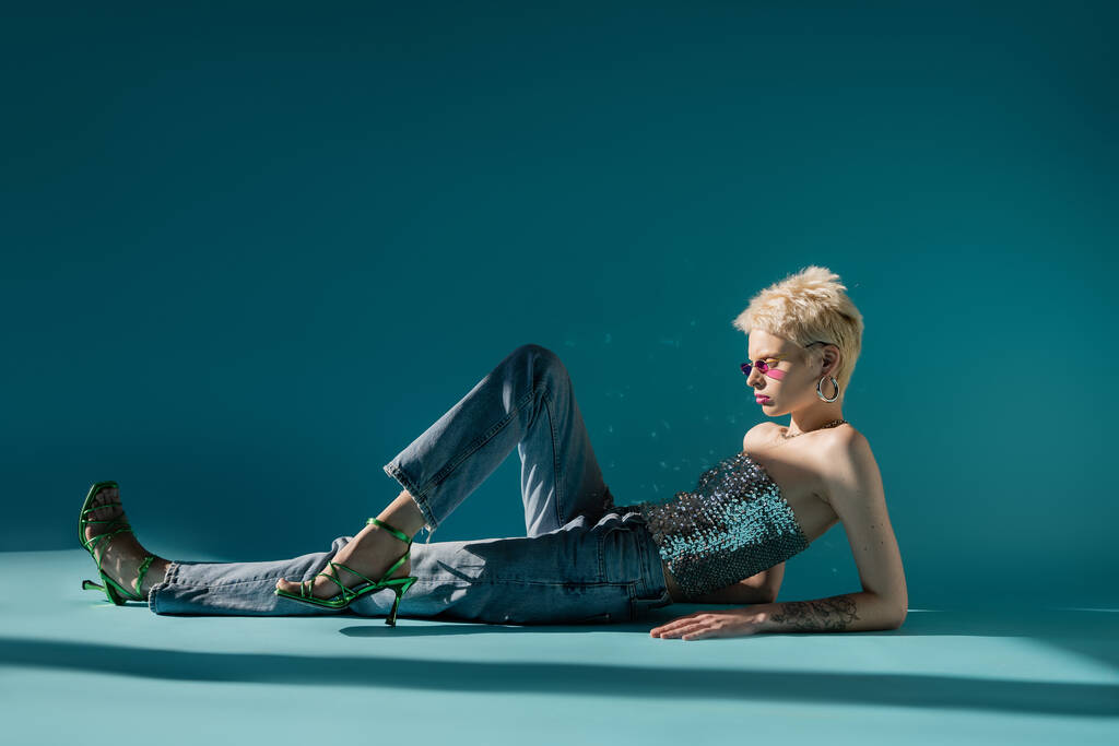 widok z boku tatuaż albinos model w różowe okulary przeciwsłoneczne pozowanie w modny strój na niebiesko  - Zdjęcie, obraz