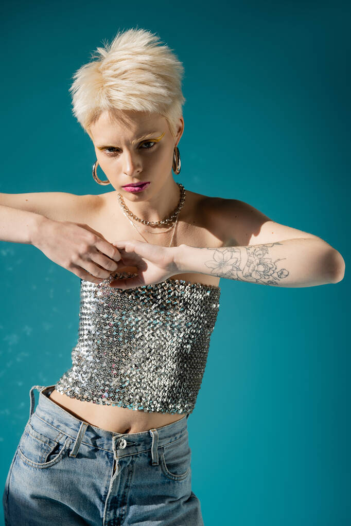 tattooed albino model in fashionable outfit looking at camera on blue background  - Photo, Image