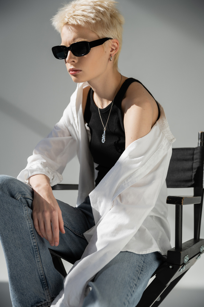 blondi nainen trendikäs aurinkolasit ja tyylikkäät vaatteet istuu taittuva tuoli harmaa  - Valokuva, kuva