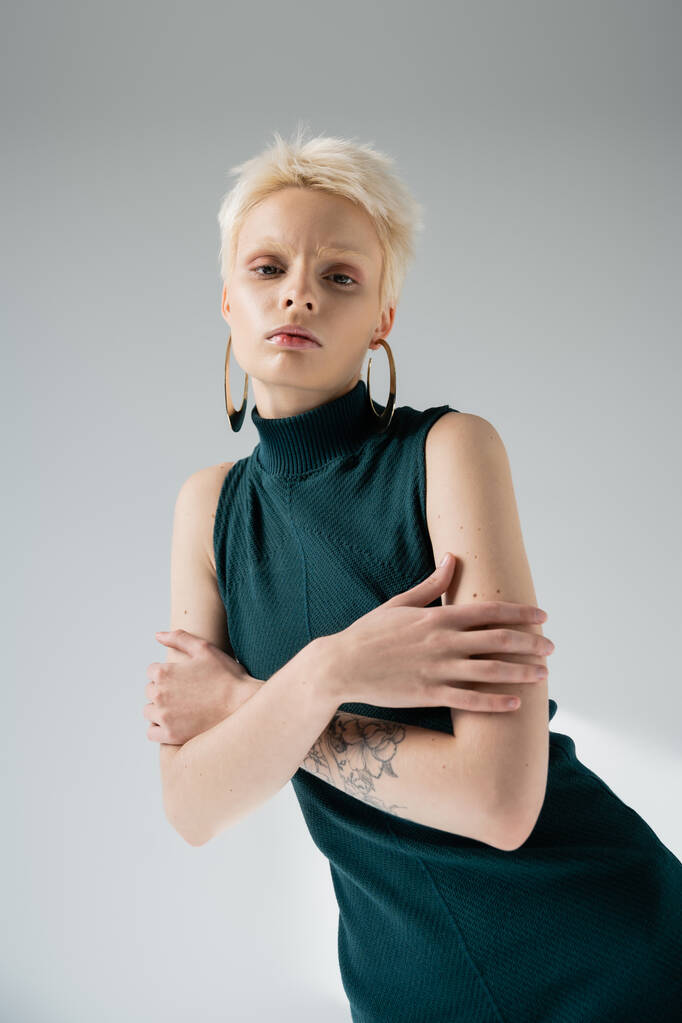 татуированная альбиноса в обтягивающем платье обнимающая себя на сером фоне  - Фото, изображение
