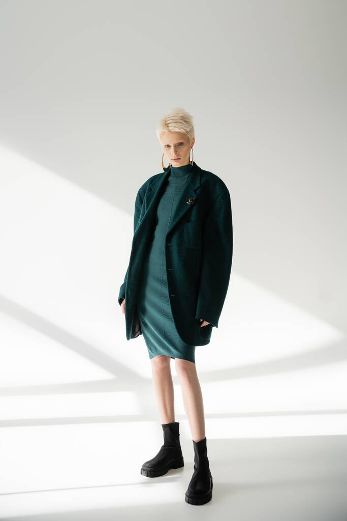 full length of young albino woman with fair-skin posing in green dress and coat on grey background  - Photo, Image