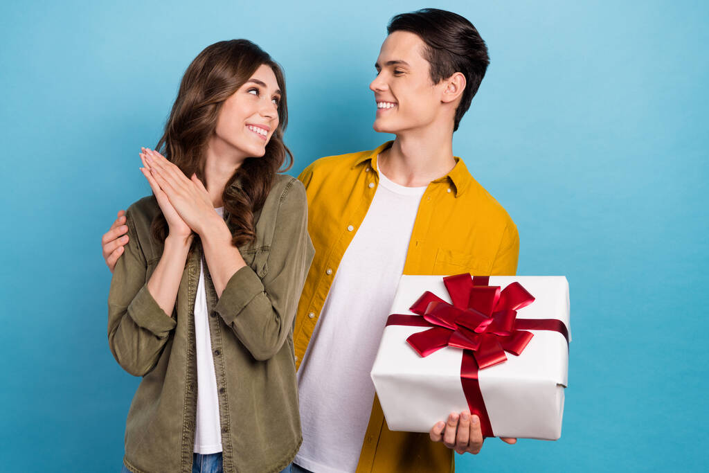 Photo of pretty cute smile couple hugs look each other hold wrapped present girlfriend with boyfriend marriage day isolated on blue color background. - Photo, Image