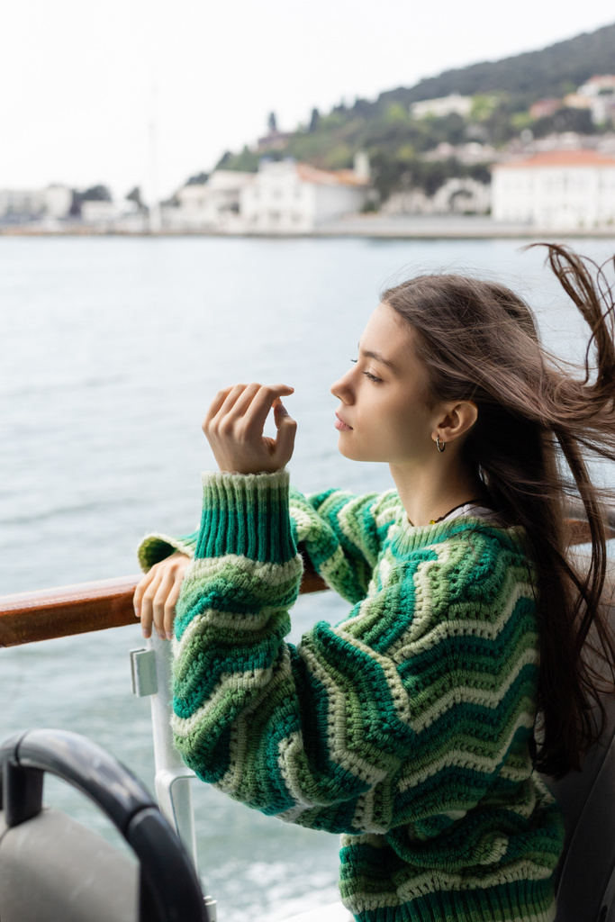 Boční pohled mladé ženy ve svetru stojící u zábradlí na jachtě v Turecku  - Fotografie, Obrázek