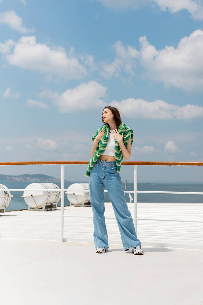 Giovane donna in maglione e jeans in piedi su traghetto con mare sullo sfondo in Turchia  - Foto, immagini