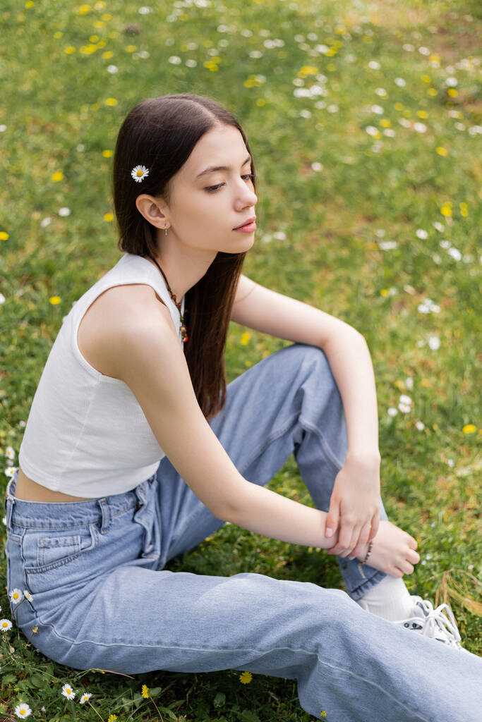 Junge Frau mit Blume im Haar sitzt auf Rasen im Park  - Foto, Bild