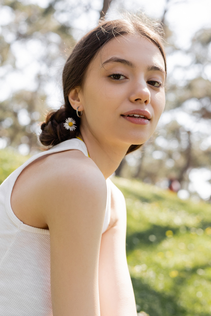 Retrato de mulher jovem com flor no cabelo olhando para a câmera no parque  - Foto, Imagem