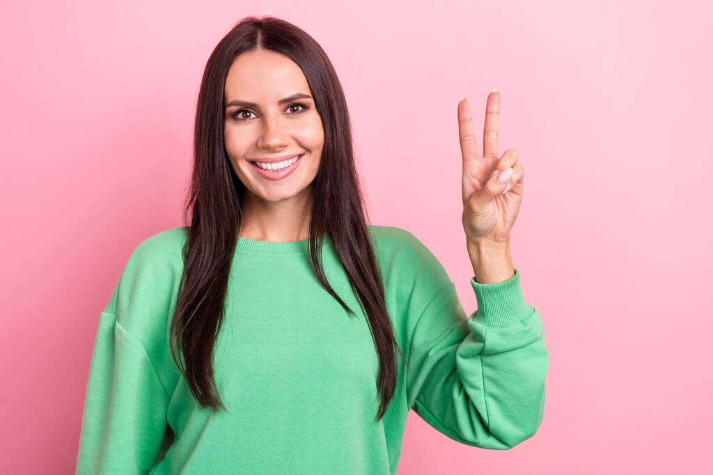 Портрет очаровательной красивой улыбки латинская молодая женщина носить зеленую стильную рубашку показывая палец V-знак привет символ изолирован на розовом фоне цвета. - Фото, изображение
