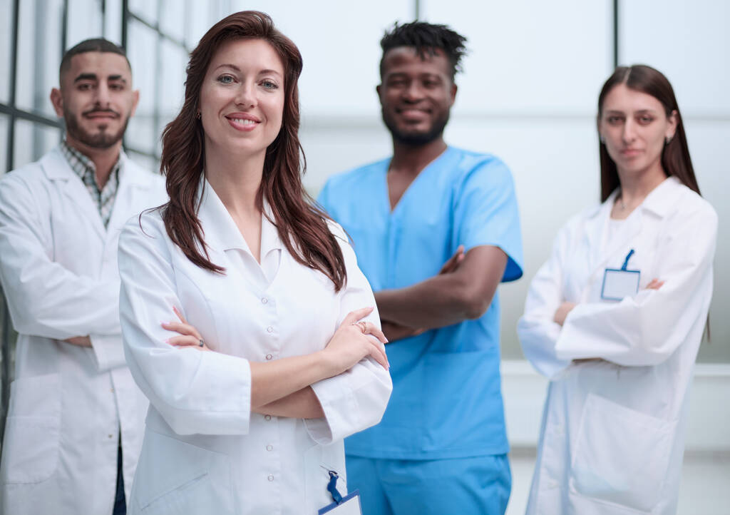Un gruppo multietnico di quattro medici e infermieri in piedi in un corridoio ospedaliero indossando abiti e camici. - Foto, immagini