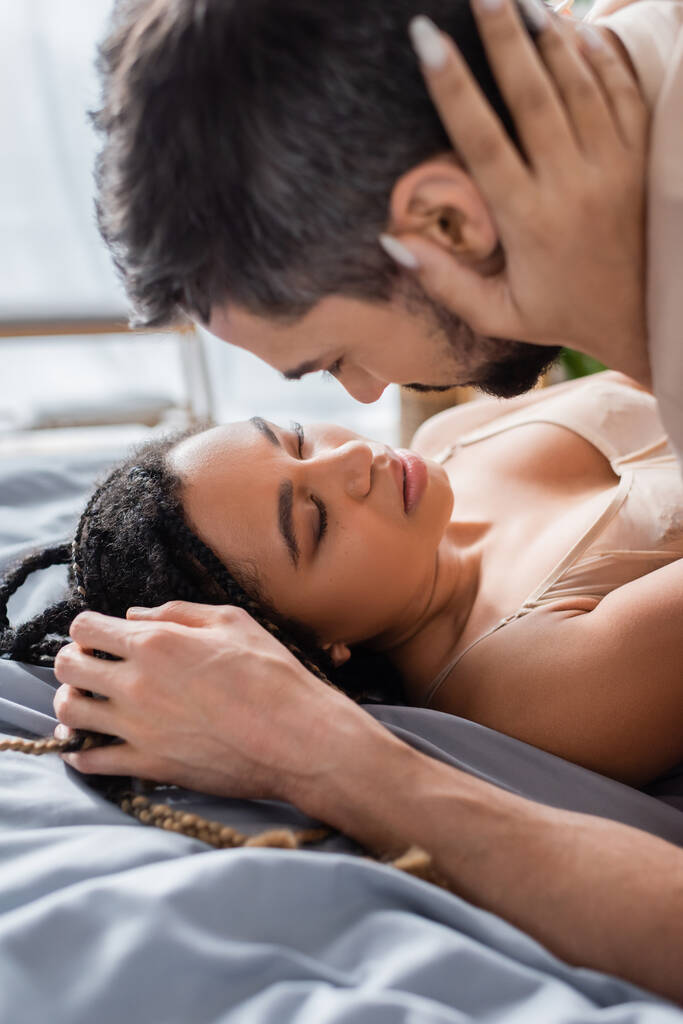 sexy african american woman in lingerie embracing blurred man on bed at home - Photo, Image