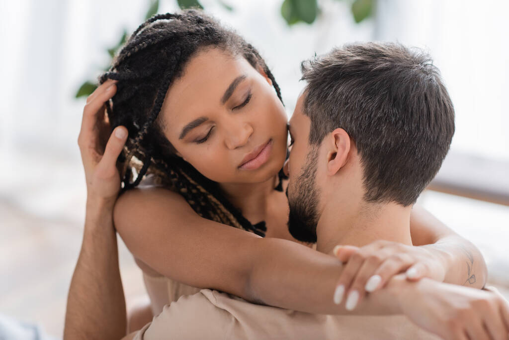 Genç ve seksi Afro-Amerikan kadın gözleri kapalı ve sarılan esmer adam evde. - Fotoğraf, Görsel