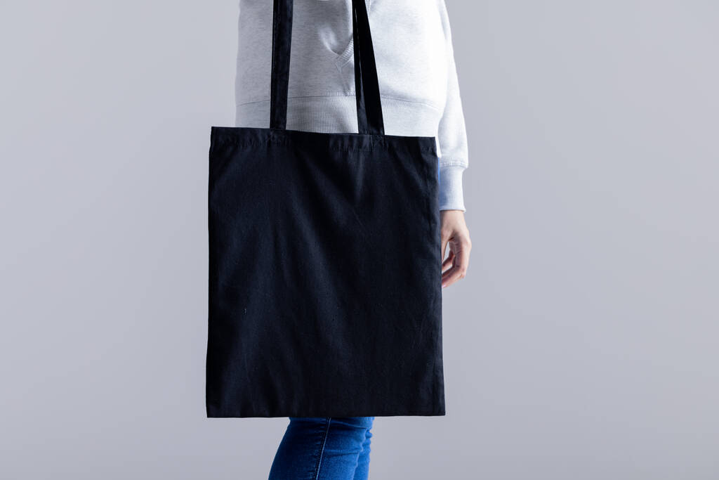 Mulher caucasiana segurando saco de lona preta com espaço de cópia em fundo cinza. Sacos e conceito de moda. - Foto, Imagem