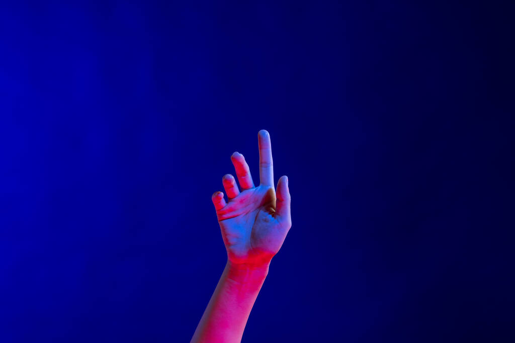Odhalená ruka ukazující prstem ve studiu s modrým světlem s kopírovacím prostorem. Virtuální realita a technologie digitálního rozhraní. - Fotografie, Obrázek