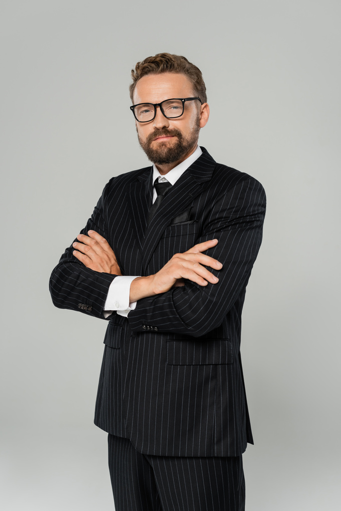 vrolijke zakenman in formele kleding en bril poseren met gekruiste armen geïsoleerd op grijs  - Foto, afbeelding