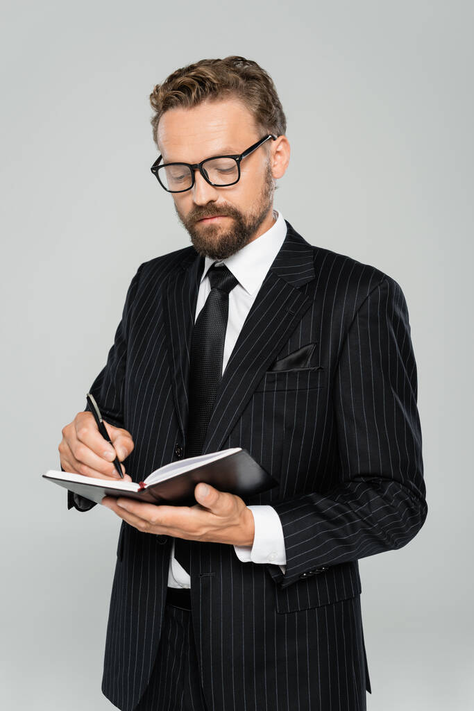 dobře oblečený podnikatel v brýlích a formální oblečení psaní v notebooku izolované na šedé  - Fotografie, Obrázek