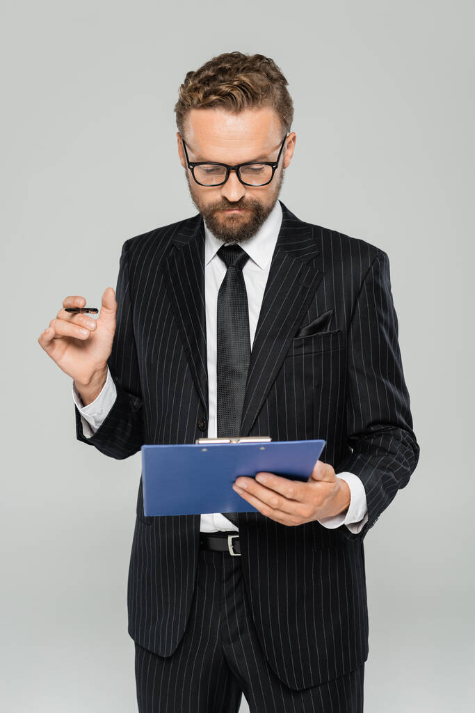 gut gekleideter Geschäftsmann mit Brille und formaler Kleidung, Klemmbrett mit Stift isoliert auf grau  - Foto, Bild