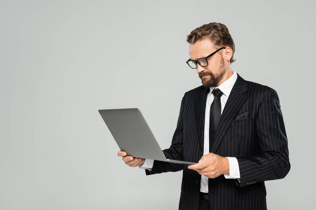 well dressed businessman in glasses using laptop isolated on grey  - Photo, Image