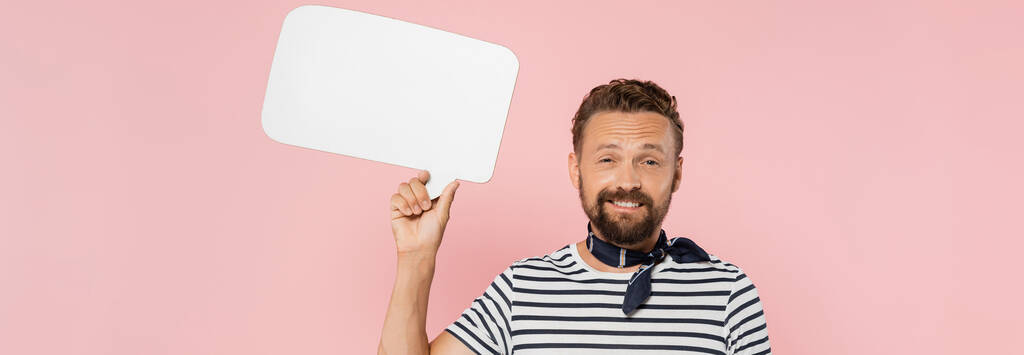 happy french guy in striped t-shirt and neck scarf holding speech bubble isolated on pink, banner  - Photo, Image