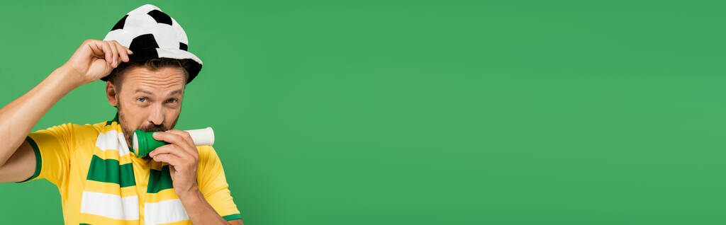 Futbol şapkalı sakallı adam kornaya basarken yeşil pankartta yalnız başına tezahürat yapıyor.  - Fotoğraf, Görsel