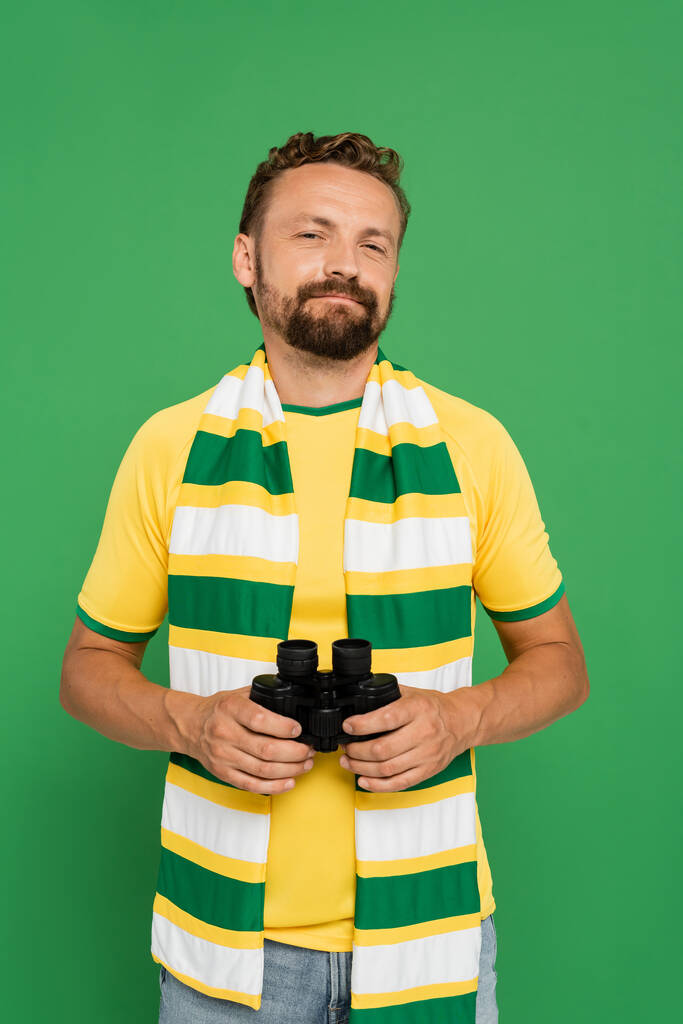 Futbol maçında elinde dürbün tutan çizgili fularlı sakallı bir adam yeşil alanda izole edilmiş. - Fotoğraf, Görsel