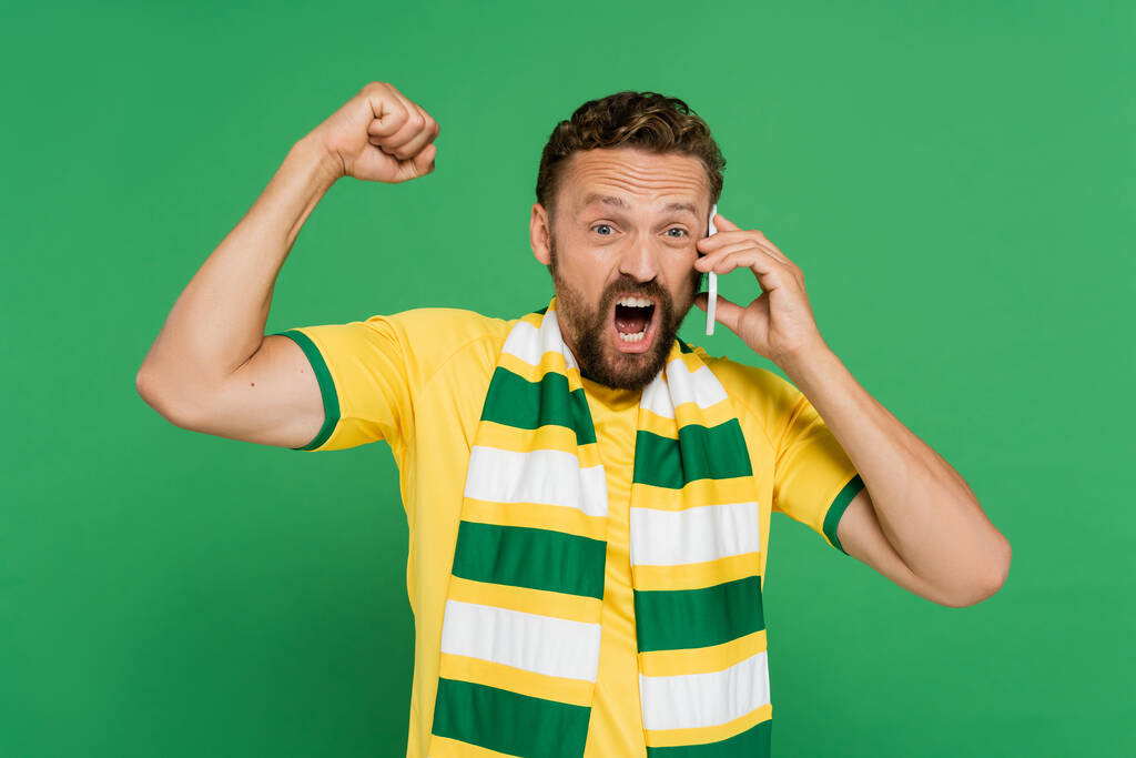 эмоциональный мужчина в полосатом шарфе кричит во время разговора на мобильном телефоне изолирован на зеленый - Фото, изображение