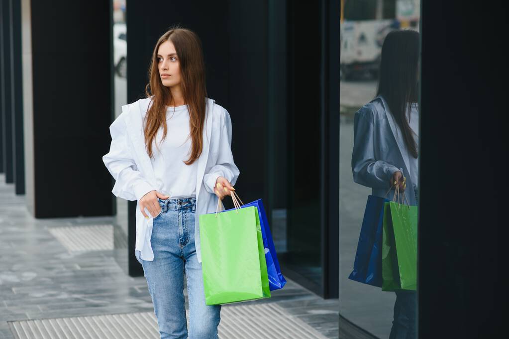 Lüks marka alışveriş torbaları taşıyan bir kadın, alışveriş merkezinin yakınında yürüyor.. - Fotoğraf, Görsel