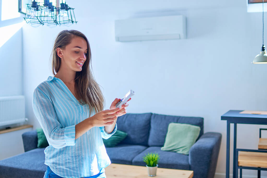 Junge nette, lässige Frau mit Klimaanlage und Anpassung der angenehmen Temperatur mit Fernbedienung in der Wohnung - Foto, Bild